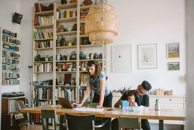 Woman using laptop while young man playing with daughter at table in house