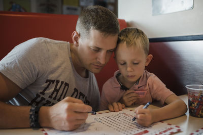 Father with son solving puzzle while sitting in restaurant