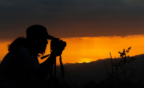 Silhouette person photographing against sky during sunrise