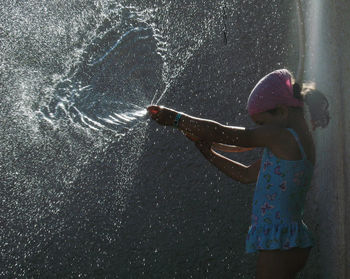 Girl in swimwear playing with hose against wall