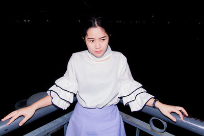 Thoughtful young woman standing against railing at night