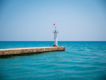 Lighthouse by sea against clear sky