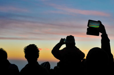 Rear view of people taking picture at sunset