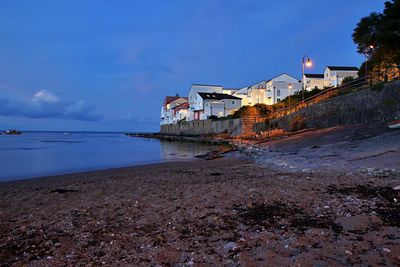 Illuminated buildings by sea against sky at night