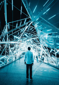 Rear view of man standing on illuminated ceiling