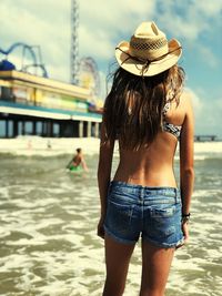 Rear view of woman in hat standing at beach