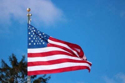 Low angle view of american flag waving against blue sky