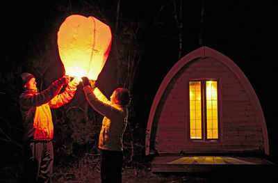 People standing by illuminated lantern at night