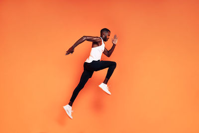 Full length of man jumping against orange background