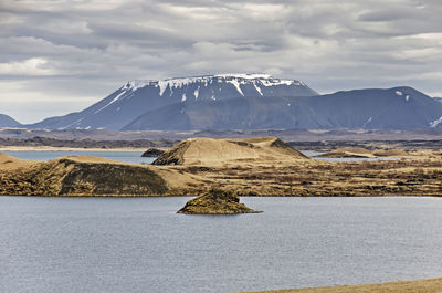 View across a lake towards a small island, a pseudocrater and a mountain range in iceland