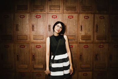 Portrait of young woman standing against lockers