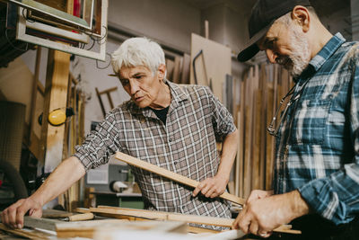 Male carpenter explaining colleague while working together at repair shop