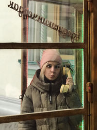 Young woman standing in telephone booth seen through glass