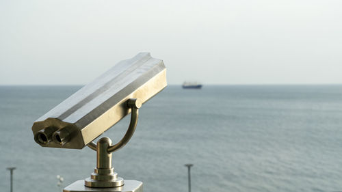 Close-up of coin-operated binoculars against sea during sunset