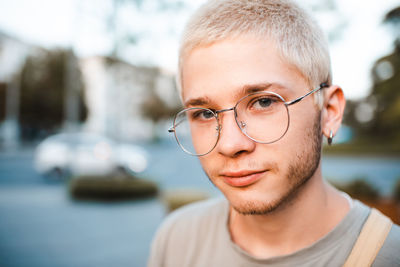 Handsome young man with blond short cut hairstyle wear glasses over urban city background outdoor. 