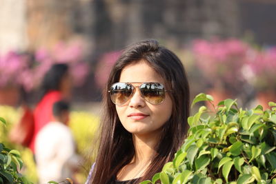 Portrait of young woman wearing sunglasses while standing against trees