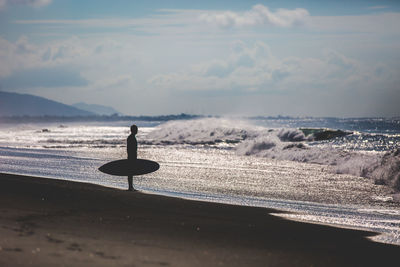 Silhouette of surfer on beach against sky