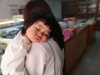 Mother carrying cute sleeping baby girl while standing in store