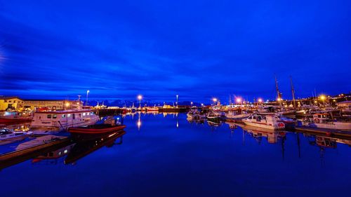 Boats moored at harbor against cloudy blue sky