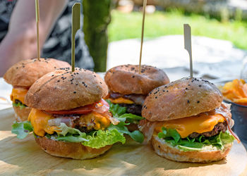 Close-up image of delicious burgers on wooden board on table in back yard.