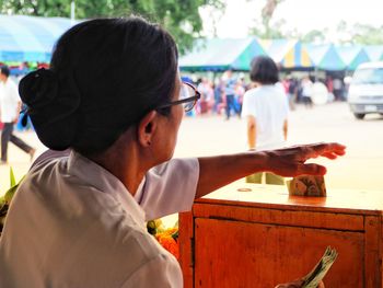 Rear view of woman inserting money in donation box