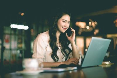 Young woman using mobile phone while sitting on table