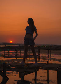 Silhouette mid adult woman standing at beach against orange sky during sunset