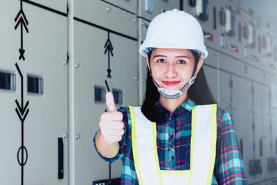 Portrait of female worker gesturing while standing by electrical fuse