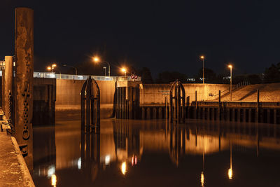 Illuminated street lights by river against sky at night