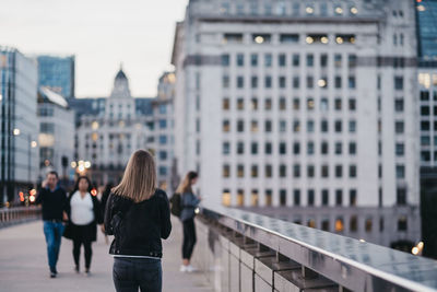 Rear view of people walking on railing against buildings in city