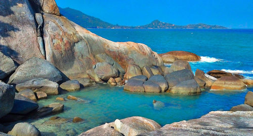 Rock formations by sea against blue sky