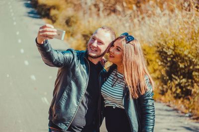 Happy couple taking selfie on road during sunny day
