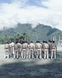 Rear view of police standing on road against cloudy sky