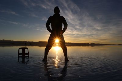 Silhouette man standing in lake against sky during sunset