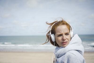 Redheaded woman relaxing at the beach, listening music with headphones