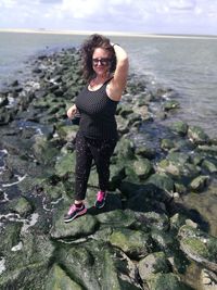 Young woman standing on rock at sea shore against sky