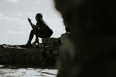 Woman sitting on rock against sky