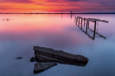 Wooden posts on lake against sky during sunset