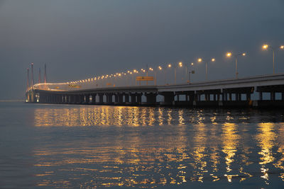 Illuminated bridge over river against sky during sunset