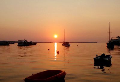 Sailboats moored on sea against sky during sunset