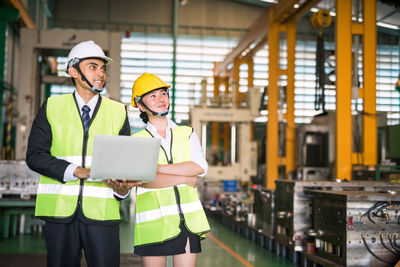 Engineers holding laptop looking away in factory