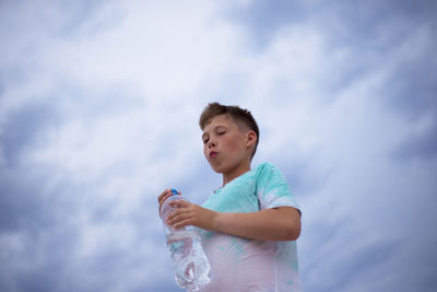 Boy with a bottle of clean water on the background of the sky. thirst. drink water.