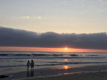 Silhouette people on beach against sky during sunset