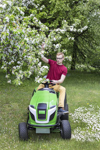 Man driving lawn mower by trees on grassy field