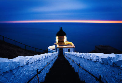 Illuminated building by sea against sky at dusk