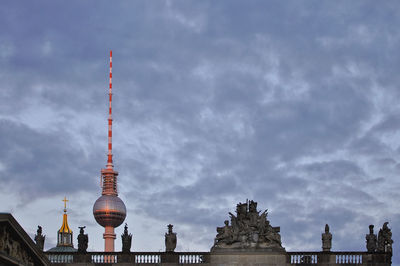Low angle view of fernsehturm tower against cloudy sky at dusk in city