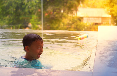 Boy play water with funny face near poolside in swimming pool in summer vacation