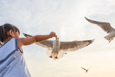 Low angle view of birds flying over girl against sky