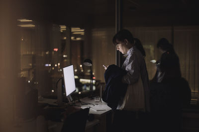 Businesswoman using smart phone while working late in office at night