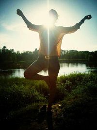 Silhouette of man with arms outstretched standing on lake at sunset